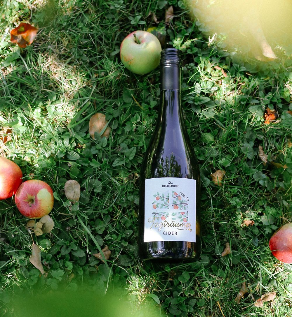 Eine Flasche Apfel-Cider mit dem gestalteten Etikett von Katharina Damm Kreativstudio mitten im Gras unter dem Apfelbaum. 