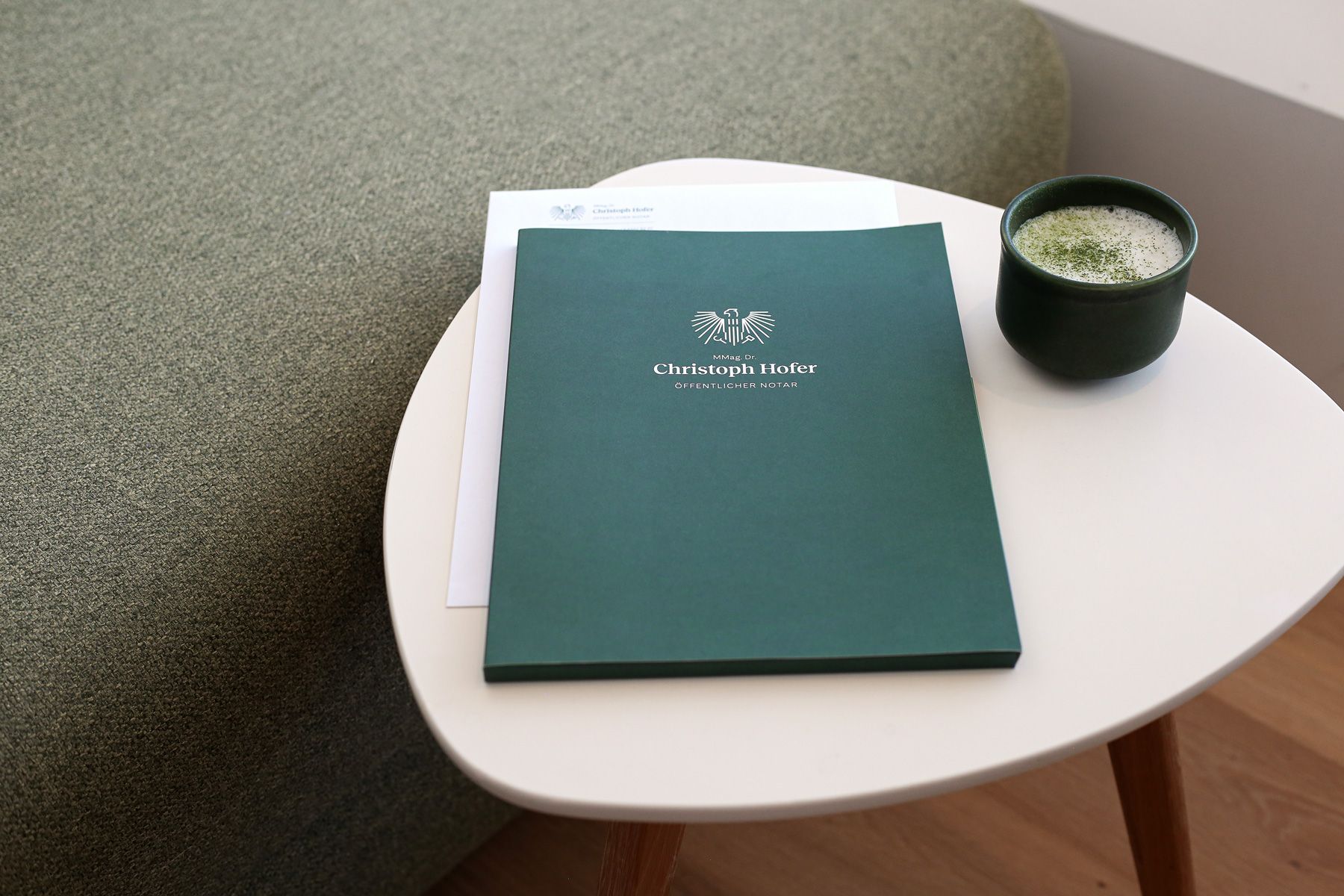 Flügelmappe im neuen Corporate Design für das Notariat in Mittersill im Salzburger Land liegt auf einem Tisch neben einem Match Latte - farblich abgestimmt.